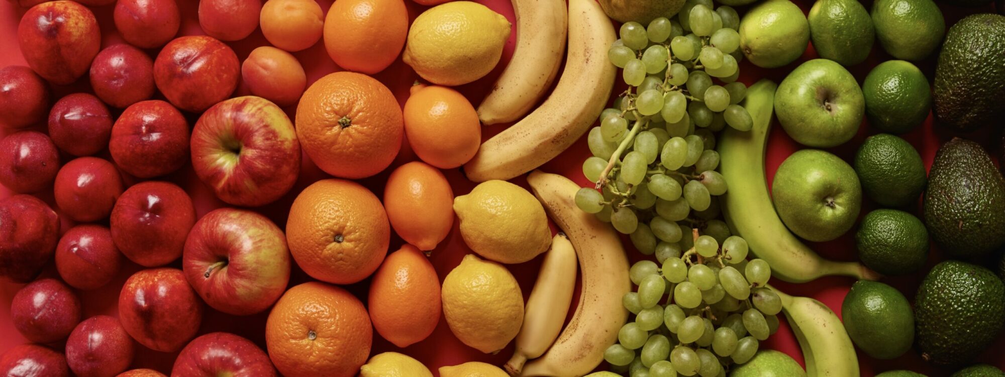 Assorted healthy citrus fruits on bright red background. Ripe peaches, apples, oranges, bananas, grapes and avocado for your healthy nutrition. Set of nutritious food. Balanced diet, clean eating.